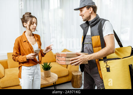 Bello corriere in uniforme garantendo la pizza con borsa termica per un client home, donna felice ricevere il suo ordine Foto Stock