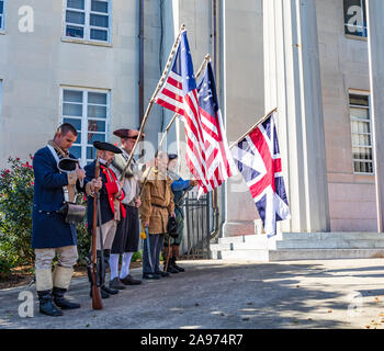 LINCOLNTON, NC, Stati Uniti d'America-11 NOV 2019: una linea di uomini vestiti in periodo negli Stati Uniti costume militare, tenendo bandiere storiche, con testa inchinata nella preghiera. Foto Stock