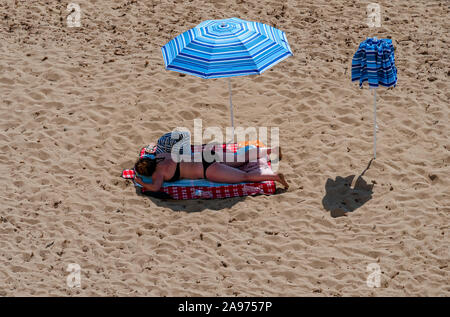 Donna di mezza età che giace all'ombra di un ombrellone sulla spiaggia del porto del Mediterraneo presso il mare blu profondo Foto Stock