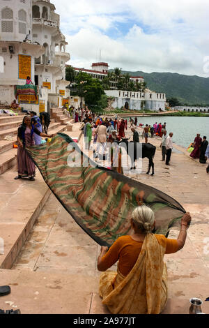 Pushkar, Rajasthan, India: due donne indiane soffiare sari bagnato sulle rive (ghat) del santo lago Pushkar Foto Stock