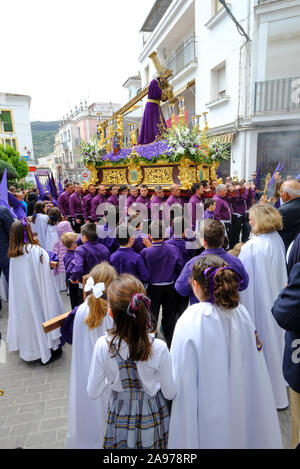 Processione della comunità locale che indossa i capiroti viola, portando Gesù e la Croce durante la settimana Santa. Carcabuey, Provincia di Cordova, Andalusia. Spagna Foto Stock