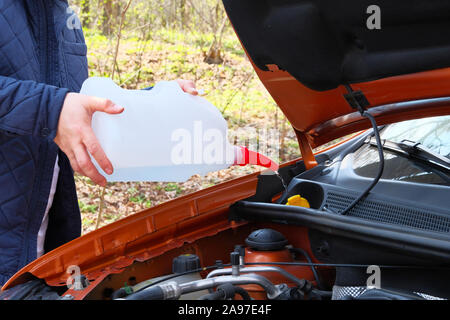 Auto il concetto di manutenzione. Il riempimento del liquido lavacristalli su auto. Driver con liquido lavavetri nelle sue mani, vicino. Foto Stock