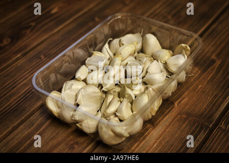 Primo piano della varietà bianca spicchi di aglio ( Allium sativum ), piantine preparate per la semina autunnale, aglio in un vassoio di plastica su sfondo di legno. Foto Stock