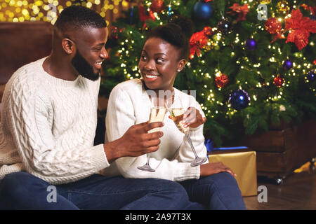 Cheers. Felice coppia nero bevendo champagne nei pressi di albero di Natale a casa vacanze di tostatura. Foto Stock