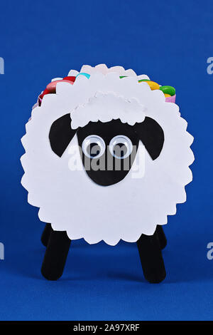 Fai da te l'Eid Al Adha agnello pecore caramella dolce carta, i bastoncini di legno per gelato su sfondo blu. Idea regalo, e il decor e l'Eid Al Adha. Procedimento kid bambini craft Foto Stock