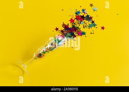 Vista superiore piatta champagne laici con vetro colorato coriandoli stelle su sfondo giallo Foto Stock