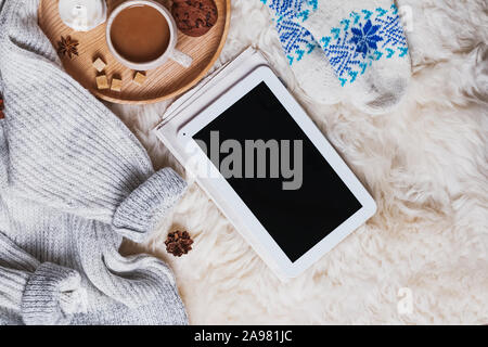 Tablet con schermo vuoto, un maglione pesante e una tazza di caffè sulla pelliccia Foto Stock