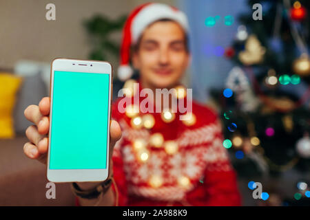 Smartphone per Natale. Uomo con telefono con schermo verde come nuovo anno presente a casa. Foto Stock