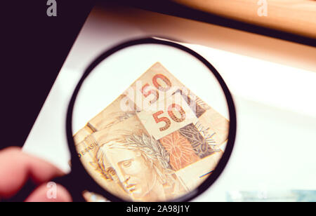 Inquadratura di un uomo con una lente di ingrandimento visualizzazione di cinquanta reais banconote, moneta brasiliana. Foto Stock