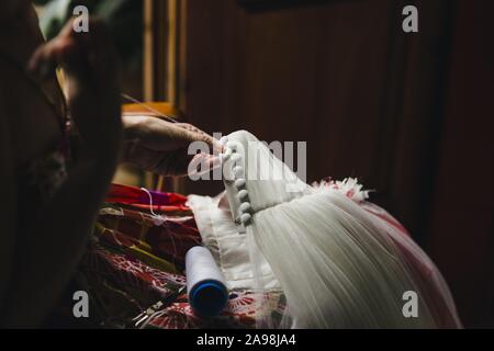 Femmina patching sarta un abito da sposa con filettatura e aghi in un modo a mano a casa. Foto Stock