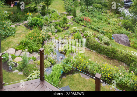 Vista dal balcone della casa di elementi di rinforzo inclinati giardino nel cortile con rock refilato stream delimitato da orange Hemerocallis - Daylily, rosa Astilbe fiori. Foto Stock