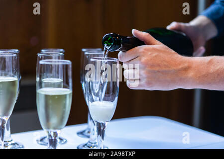 Vicino la foto di una persona di versare il vino e champagne in vuoto bicchieri di cristallo che stanno in piedi su un vestito bianco tavolo da buffet Foto Stock