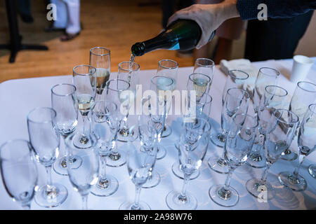 Messa a fuoco selettiva di persona il versamento di vino e champagne in bicchieri di cristallo sorge sulla sommità di un bianco tavolo da buffet Foto Stock