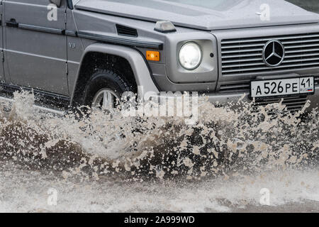 Vista ravvicinata di Mercedes-Benz G-classe, G-Wagen guida su strada allagata più profonda pozza di fango schizzi goccia di spruzzare acqua dalle ruote durante la pioggia Foto Stock