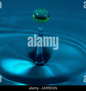 Acqua colorata scende rilasciato al momento preciso per essere catturata dalla telecamera. La bolla verde prende colore dal fondo del piatto. Foto Stock