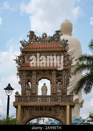 Vinh Trang Chua Tempio con un grande, bianco statua di Budda e un ornato cancello di ingresso con tante figurine di mosaico. Fotografato da dietro. Foto Stock