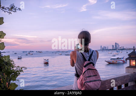 Pattaya, Tailandia - 19 Aprile 2019: bella donna prendendo una foto del tramonto. Felice giovane donna con una macchina fotografica e uno zaino. Foto Stock