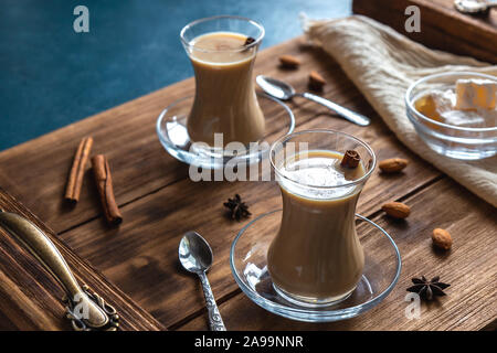 Il tè indiano con spezie e latte. Masala chai in vetri trasparenti su un vassoio in legno Orientamento orizzontale. Foto Stock