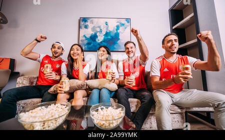 Party amici o appassionati di arsenale che guardano il calcio in tv e. Bere la birra Ganzberg festeggiando la vittoria a casa Foto Stock