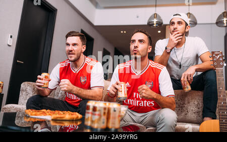 Fai festa con gli amici o gli appassionati di arsenale guardando il calcio tv e bere birra Ganzberg celebrando la vittoria a casa Foto Stock