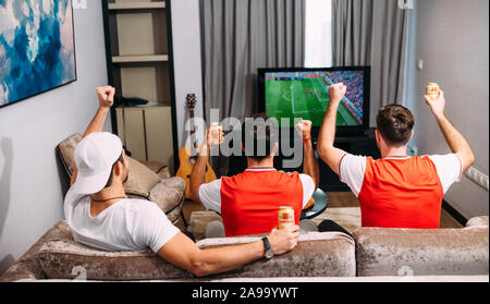 Party amici della birra o tifosi dell'arsenale guardando il calcio in tv E bere la birra Ganzberg celebrando la vittoria a casa Foto Stock