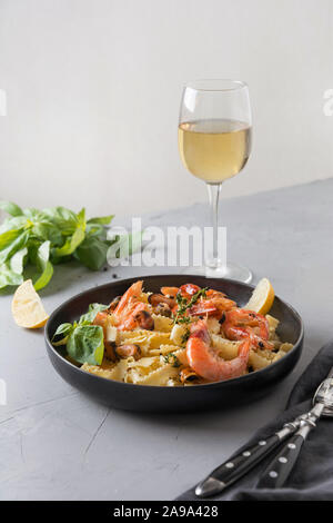 Reginelle Pasta con pesce, gamberi, cozze, bicchiere di vino bianco grigio sul tavolo di pietra, vicino. Piatto tradizionale nel ristorante italiano. Foto Stock