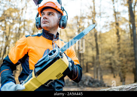 Ritratto di un professionista lumberjack in indumenti da lavoro protettiva in piedi con una motosega su una pila di registri nella foresta Foto Stock