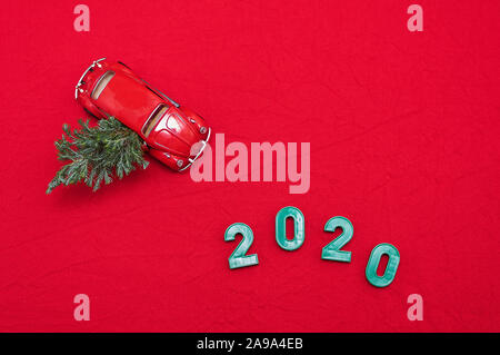 Rosso auto giocattolo con albero di Natale, l'iscrizione 2020. Rosso sfondo di Natale. Vista dall'alto. Lay piatto. Copia dello spazio. Foto Stock