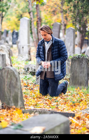 Lutto giovane uomo in ginocchio di fronte a una grave su un cimitero durante un triste giorno d'autunno. Foto Stock