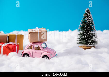 Vendita di natale. Primo piano con poco retrò auto rosa circondato da molti big giftboxes vicino sempreverde Pino banner per newyear annuncio Foto Stock