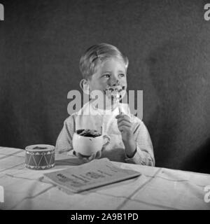 Un ragazzino di mangiare un budino di cioccolato ed è completamente cosparse, Germania 1940s. Foto Stock