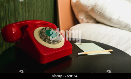 Close-up sul rosso, vintage Ricerca telefono con pulsanti nella camera di albergo con il blocco note e matita Foto Stock