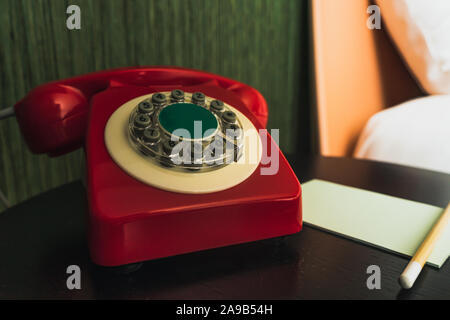 Close-up sul rosso, vintage Ricerca telefono con pulsanti nella camera di albergo con il blocco note e matita Foto Stock