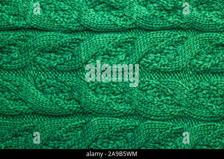 Una maglia trecce di fili verde. Un maglione di lana ornamento. Con filato a maglia. Tessitura di lana sciarpa. Abstract background tessile. Foto Stock
