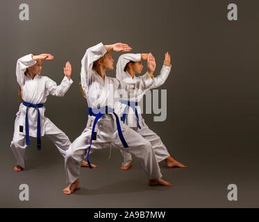 Tre piccoli karate le ragazze in un kimono bianco e blu cinghie eseguire una bella squadra kata su sfondo scuro Foto Stock