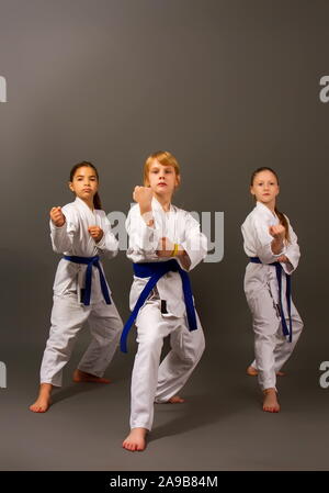 Tre piccoli karate le ragazze in un kimono bianco e blu cinghie eseguire una bella squadra kata su sfondo scuro Foto Stock