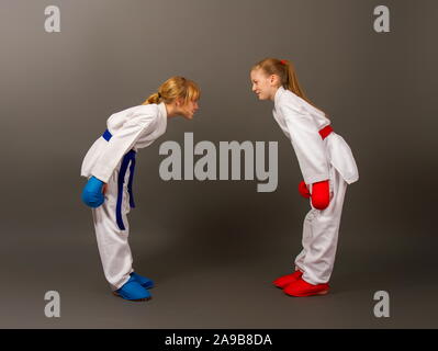 Due piccoli karate le ragazze in kimono e pieno di sport ingranaggio protettivo di rosso e blu bow gli uni agli altri come un segno di rispetto prima della lotta. Foto Stock