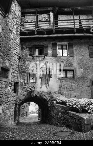 Via Fratelli Bandiera, corsia stretta attraverso archi a tunnel in colle medievale borgo di Canale di Tenno, Trentino-Alto Adige, Italia. In bianco e nero Foto Stock