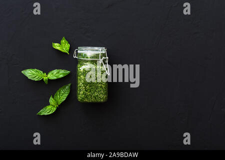 In casa il pesto e il verde del basilico sul cemento scuro dello sfondo. Verde Italia il pesto in barattolo di vetro per la pasta, spaghetti. Vegetariano cibo sano Foto Stock
