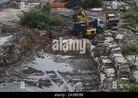 Bulldozer e del carrello durante il lavoro. Costruzione di un nuovo edificio. Fossa di grandi dimensioni con acqua. Il fango e la costruzione di macchinari. Vista da sopra. Foto Stock