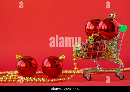 Regalo palle di Natale in una miniatura del carrello e decorazioni su uno sfondo di colore rosso. Natale e Anno Nuovo Vendita, Natale Online Store. Foto Stock
