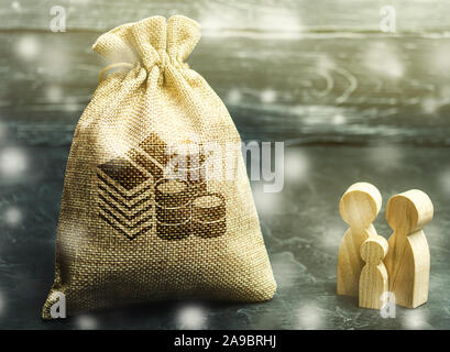 Miniatura in legno figurine famiglia stare vicino a un sacco di denaro. Il concetto di risparmio. Il Natale e le vacanze. Pianificazione del bilancio. Gestione finanziaria. Accum. Foto Stock