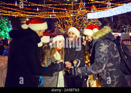 Un gruppo di amici bevendo un tè caldo in una fiera di Natale Foto Stock