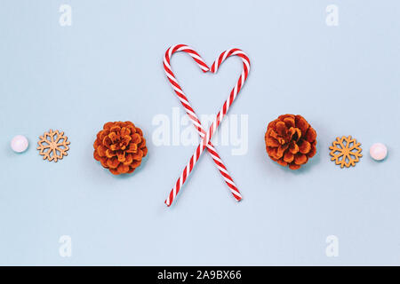 Inverno stagionali laici piana con due a strisce rosse e bianche candy canes formando la forma di un cuore, pigne, legno Ornamenti fiocco di neve e snowbal bianco Foto Stock