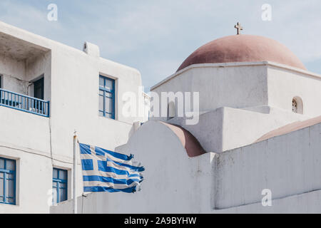 Bandiera Greca nel vento al di fuori del tradizionale chiesa con parte superiore rossa a Mykonos, Grecia. Foto Stock
