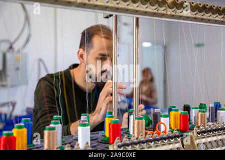 Giovane lavoratore dalla fabbrica di cucitura che dispone le bobine di filato. Bobine multicolori Foto Stock