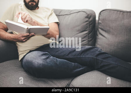 Barbuto uomo caucasico rilassante sul divano la lettura di un libro Foto Stock
