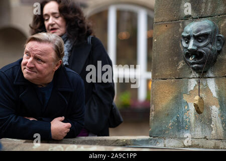 14 novembre 2019, Renania settentrionale-Vestfalia, Münster: l'attore Axel Prahl (l) si appoggia contro la fontana di fronte al Kiepenkerl, la posizione della nuova scena del crimine 'Limbus' in Münster. L'attrice Mechtild Großmann sorge nella parte posteriore. Foto: Guido Kirchner/dpa Foto Stock