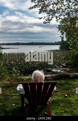 Una donna anziana si siede in una poltrona di legno in un parco vicino al fiume, Philadelphia, Pennsylvania, STATI UNITI D'AMERICA Foto Stock