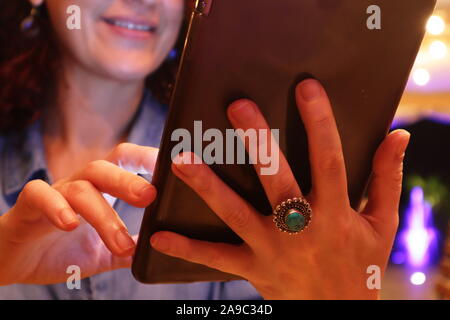 Kuwait City/Kuwait - 15/09/2019: donna che indossa Anello con ametista verde ring usando il tablet per ordinare del cibo nel ristorante dim luce Foto Stock